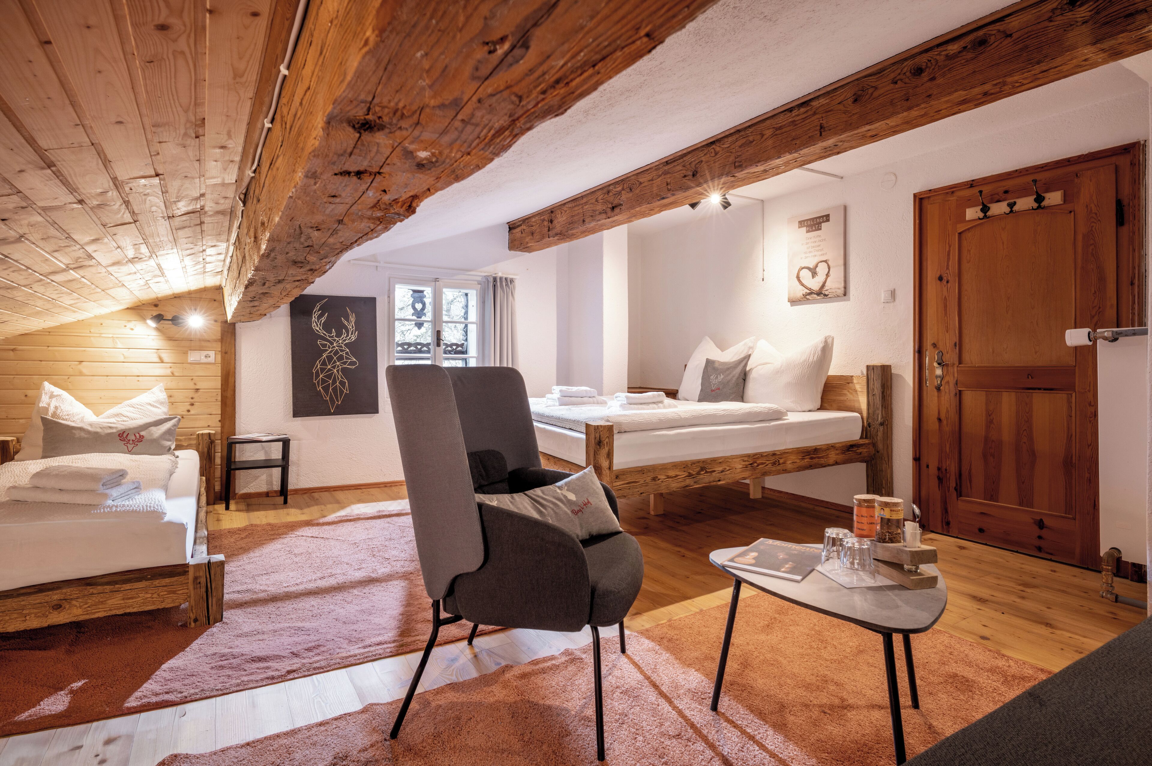Una habitación acogedora con techo de madera, una cama, una silla y una mesita con objetos encima.