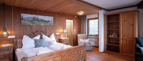 A wooden bedroom with a bed, nightstands, a chair, a wardrobe, and a painting on the wall.