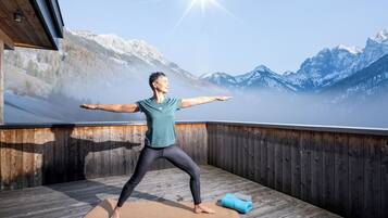 Eine Person führt eine Yoga-Pose auf einer Holzterrasse mit Blick auf die Berge aus.