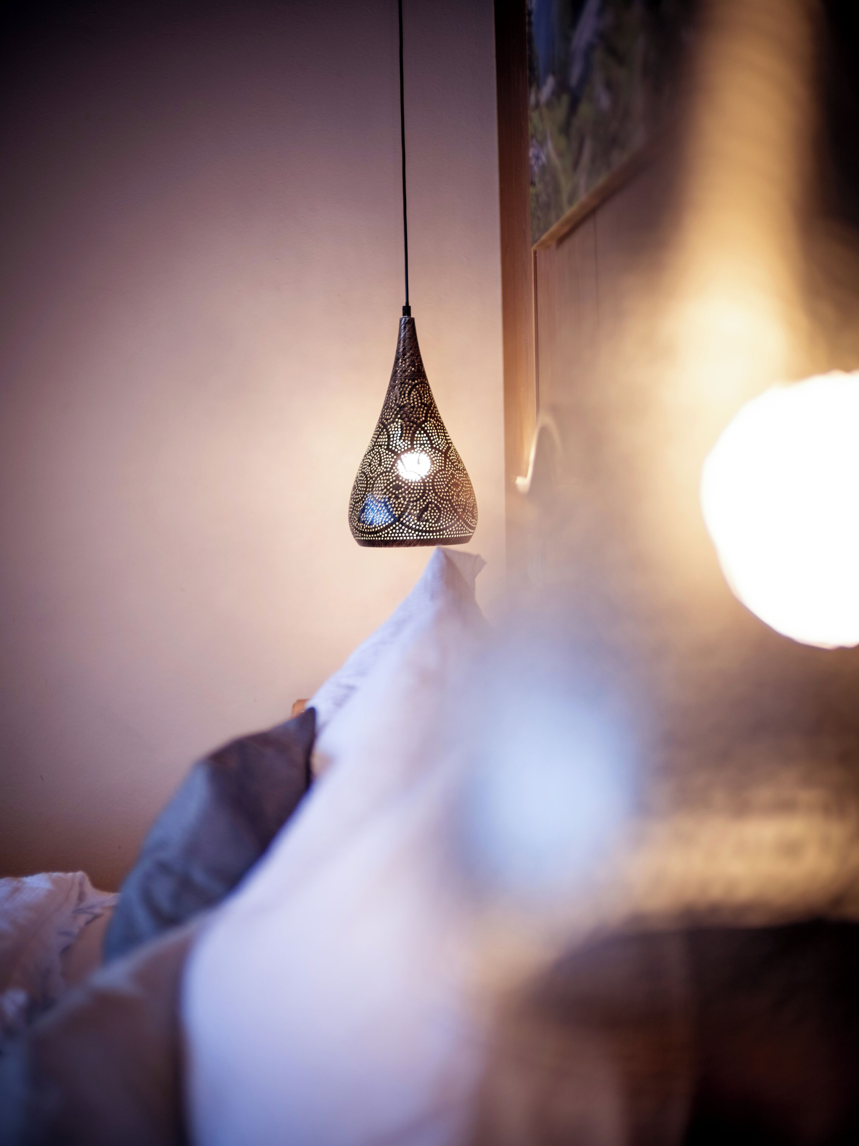 A hanging pendant light with a patterned design, a pillow, and a blurred background.