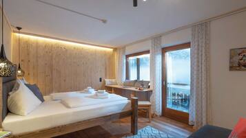 A modern bedroom with a wooden wall, a bed with white linens, a desk, and a view through a glass door.