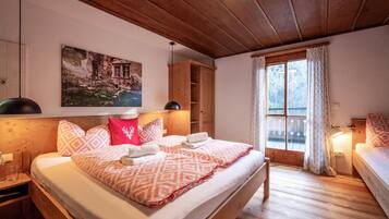 A wooden-paneled bedroom with a bed, a nightstand, a wooden wardrobe, and a window with curtains.