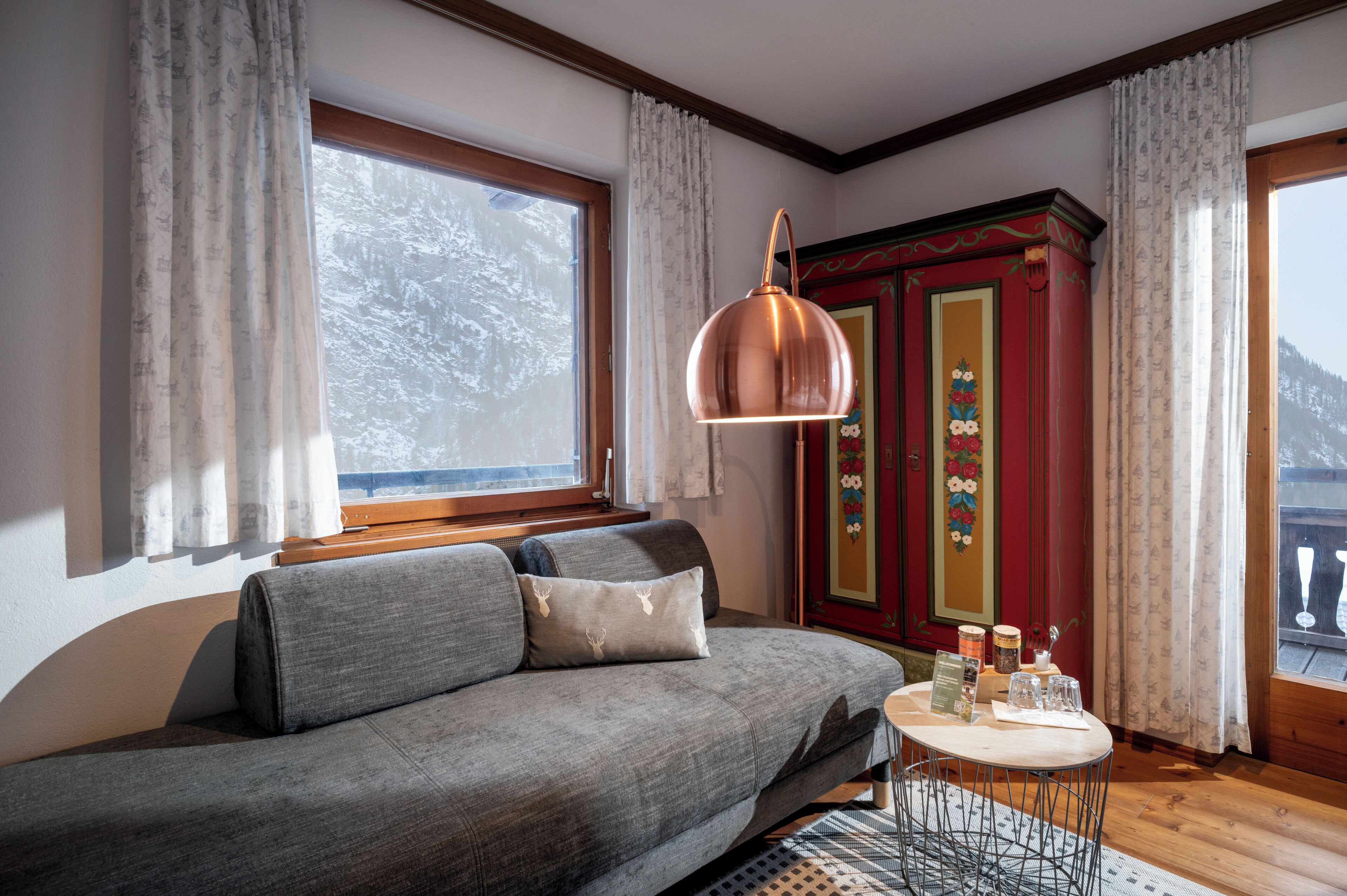 A cozy room with a sofa, a table with glasses and a menu, and a red cabinet with floral decorations.