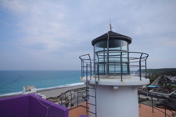 A lighthouse with a glass enclosure, overlooking a beach and ocean.