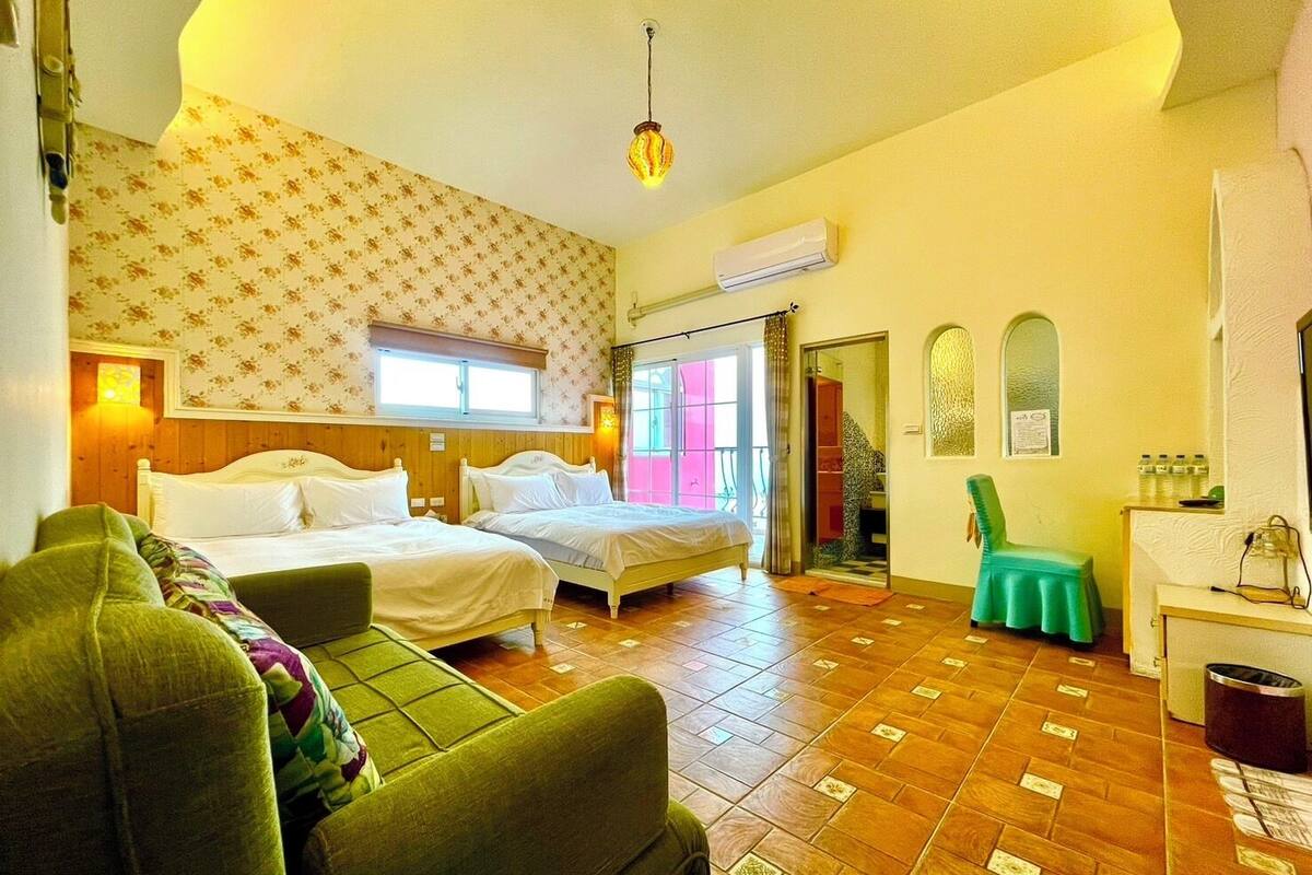 A room with two beds, a green sofa, a small table, and a window with a view.