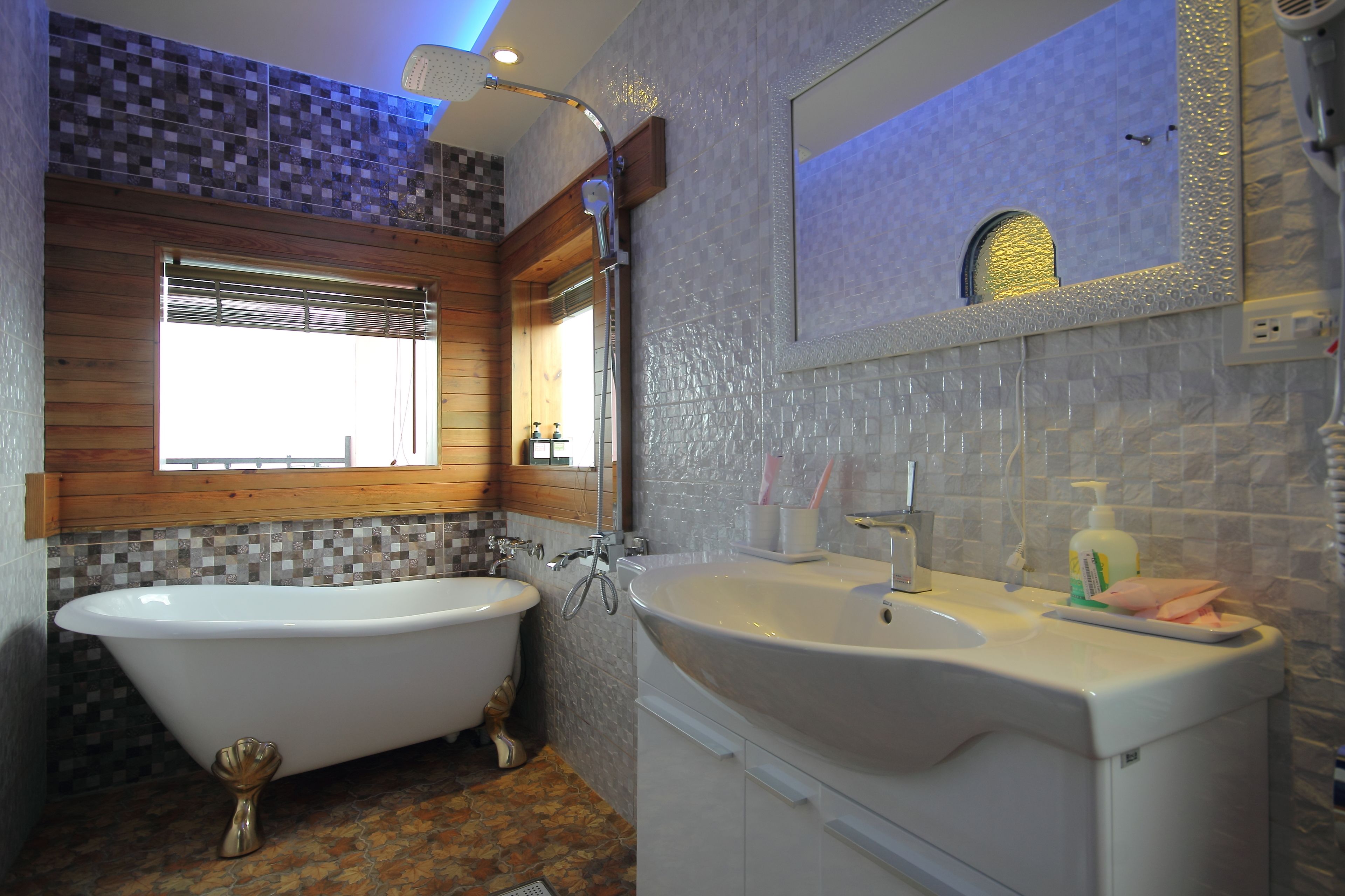 A bathroom with a freestanding bathtub, a sink with a mirror, and a window with blinds.