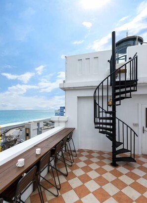 Une terrasse sur le toit avec un sol à carreaux, une table en bois entourée de chaises et un escalier en colimaçon noir.