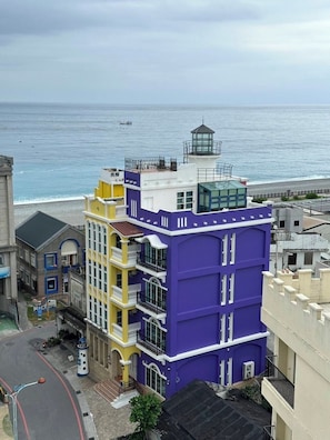 A multi-story building with a prominent purple and yellow facade, a lighthouse on top, and a view of the ocean. - Lighthouse B&B (Xincheng)