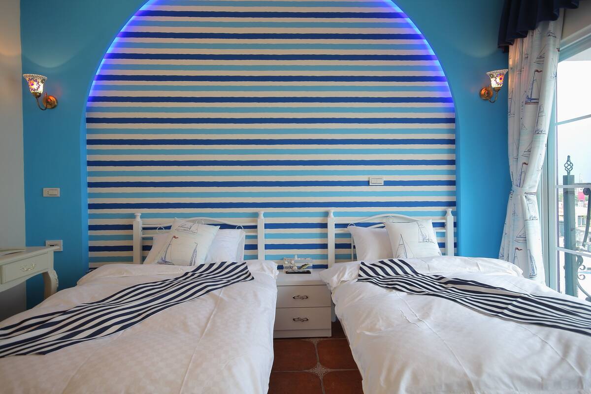 A room with two beds, a striped wall, and a window with curtains.