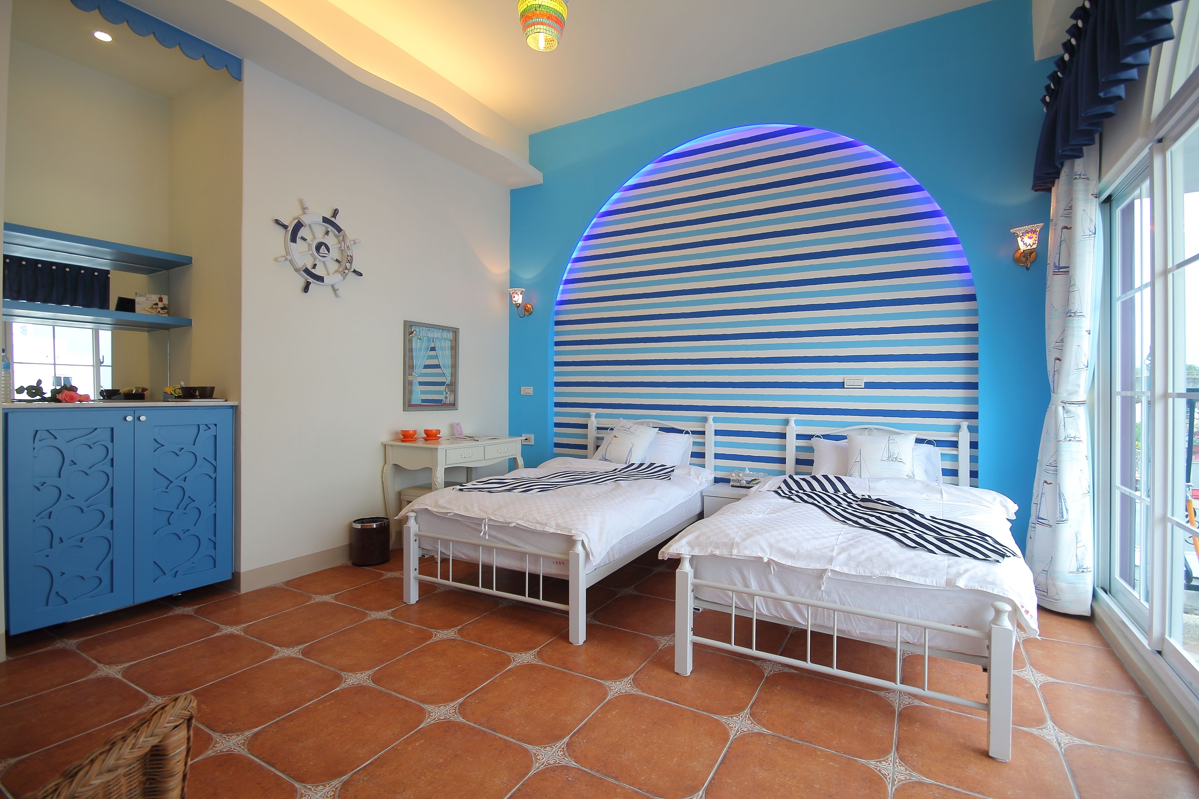 Un dormitorio con dos camas, una pared de acento azul y un ventanal grande.