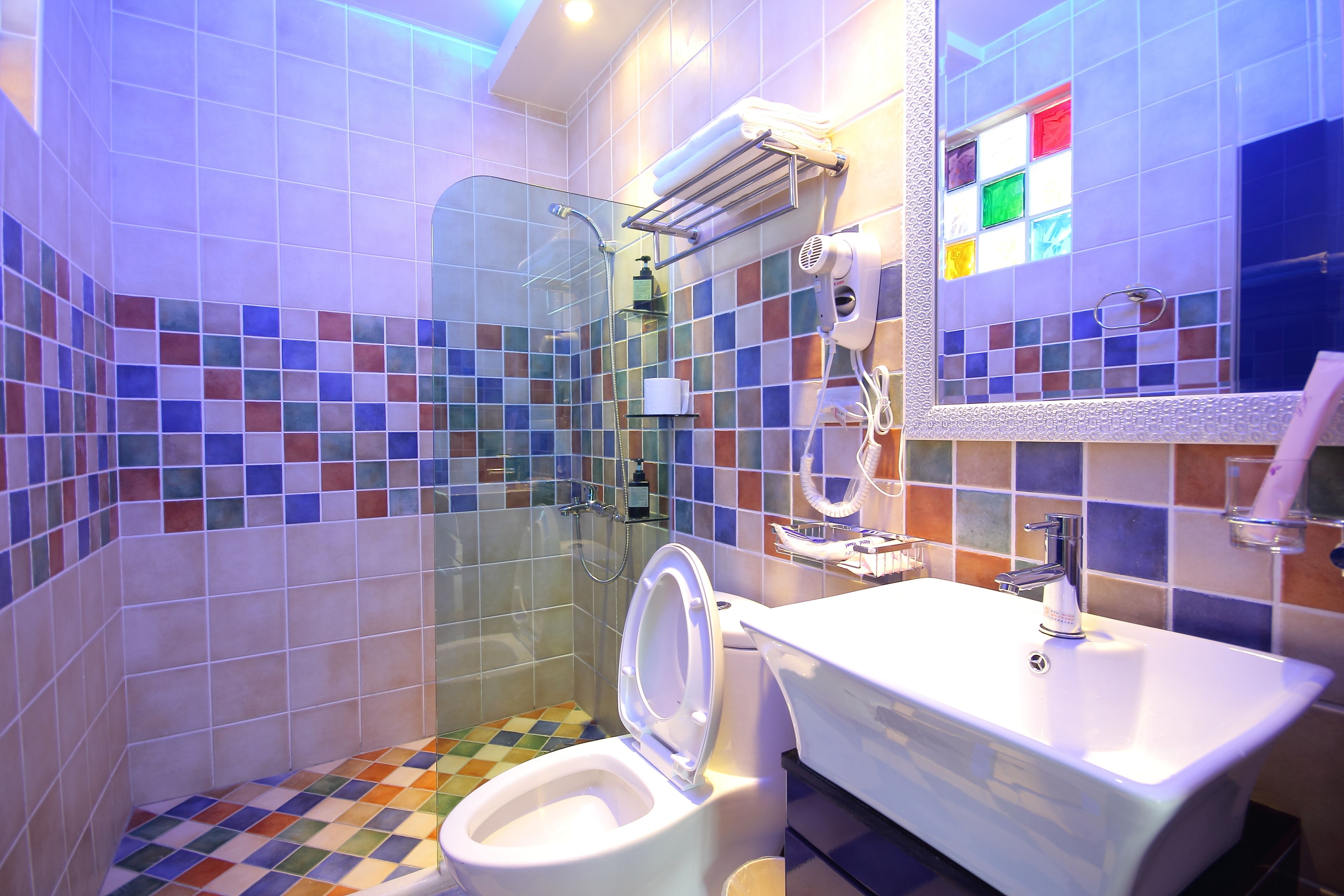 Un baño con ducha envuelta en vidrio, un lavabo blanco y un suelo de baldosas coloridas.