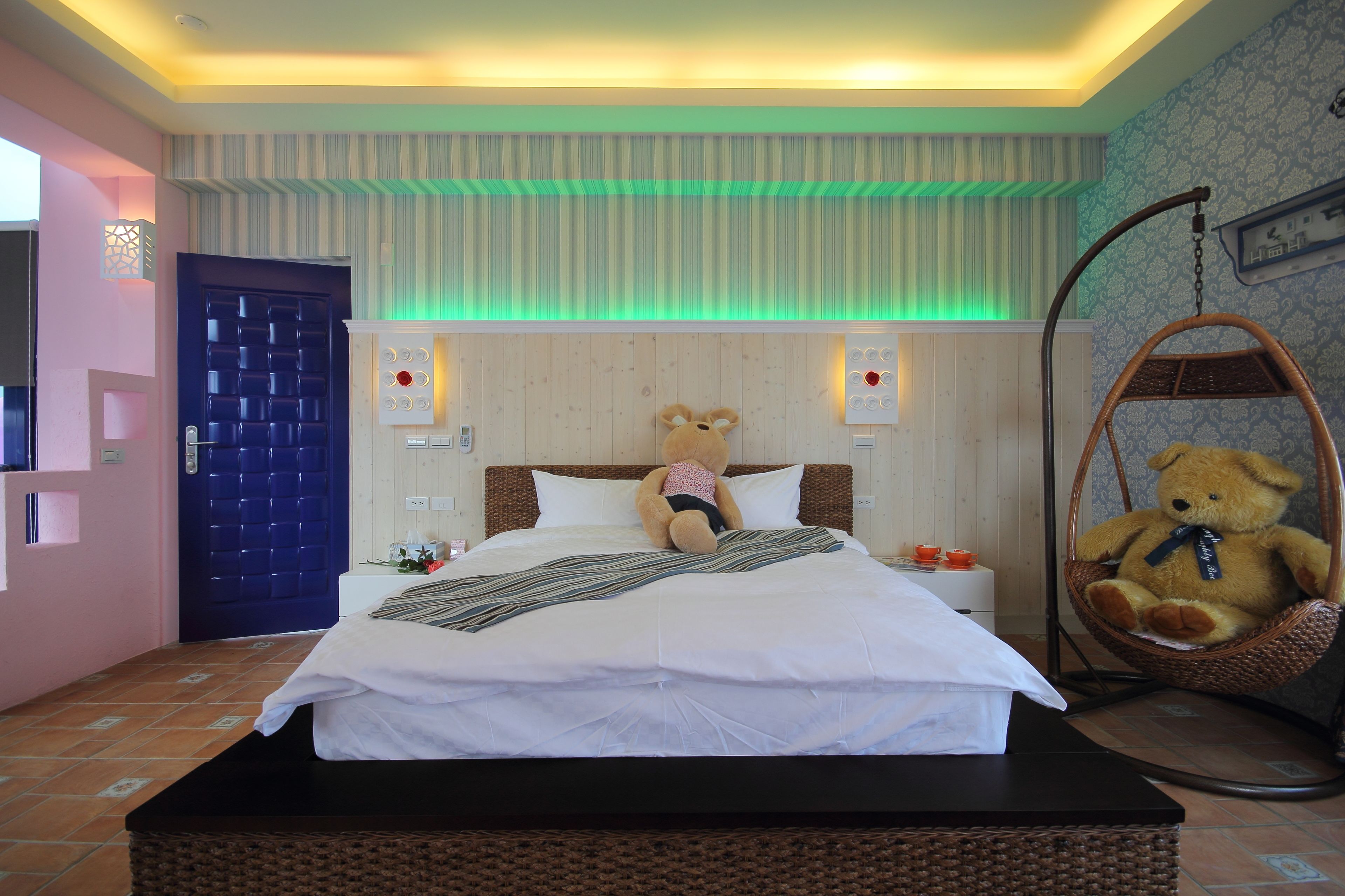 Une chambre à coucher avec un lit, un ours en peluche sur le lit, une chaise suspendue et une porte bleue.