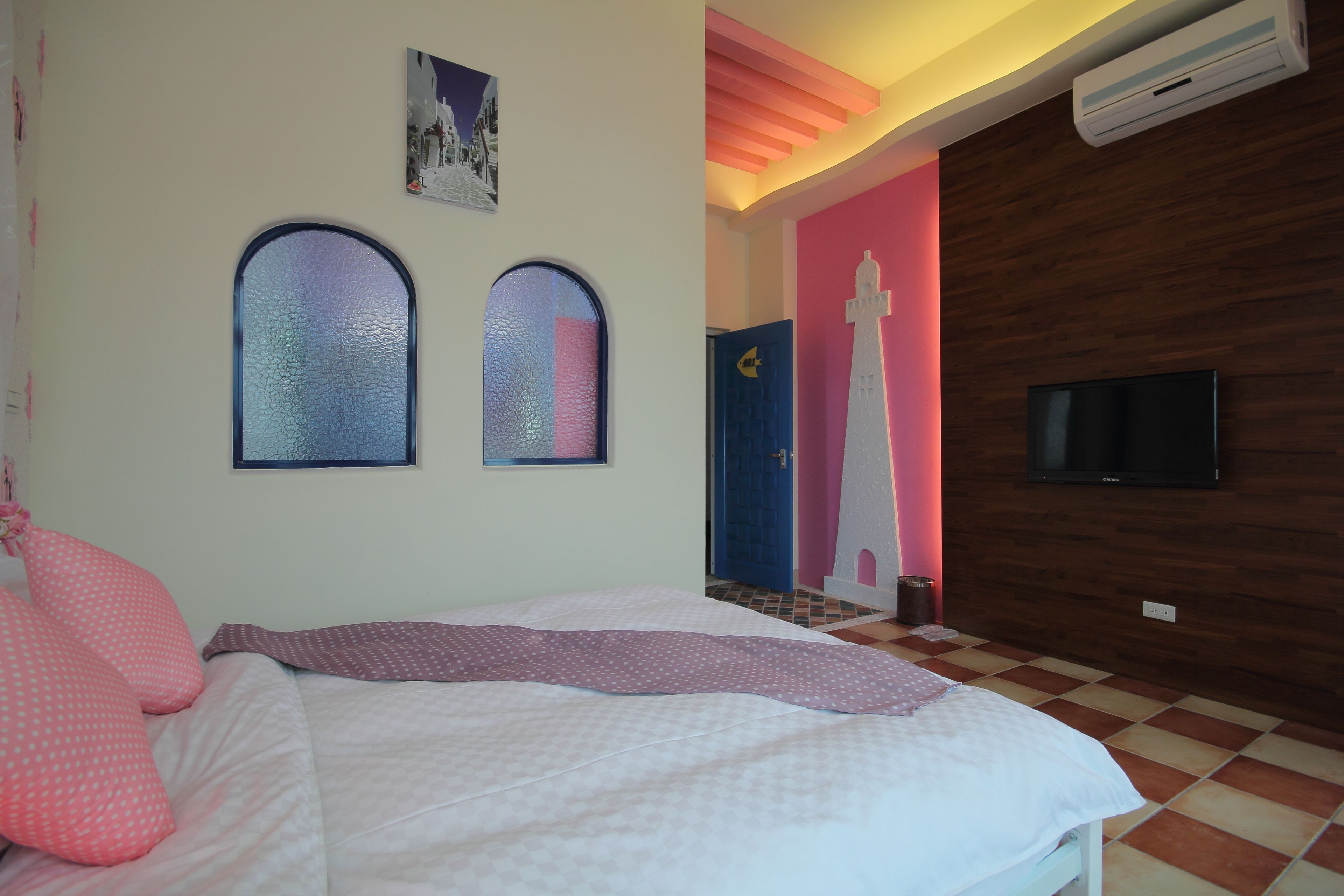 Een slaapkamer met een bed, twee boogvensters, een televisie en een houten wand.