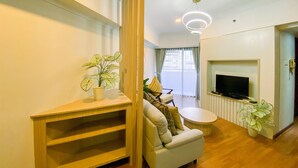 A modern living room with a sofa, a TV, a wooden entertainment unit, and a potted plant. - Cozy 2 Bedrooms Sudirman Tower Apartment by Travelio (Jakarta)
