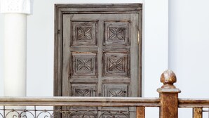 Una puerta de madera con intrincados grabados, un portón de hierro forjado y un muro blanco con un arco decorativo.