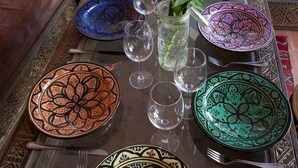 Una mesa de comedor dispuesta con platos coloridos, vasos y cubiertos, con un florero de flores y una vela en el centro.