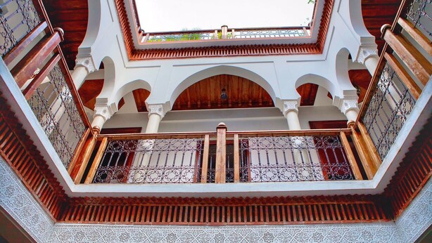 Un patio con un espacio abierto central, rodeado de arcos y columnas, y vista al cielo a través de un tragaluz.