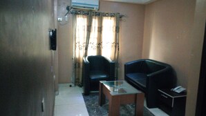 A small living room with a sofa, a glass-top coffee table, and a chair. - D'Czars Hotel & Suites (Lagos)