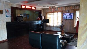 A reception area with a black counter, a television mounted on the wall, and a vase with dried plants on a table. - D'Czars Hotel & Suites (Lagos)