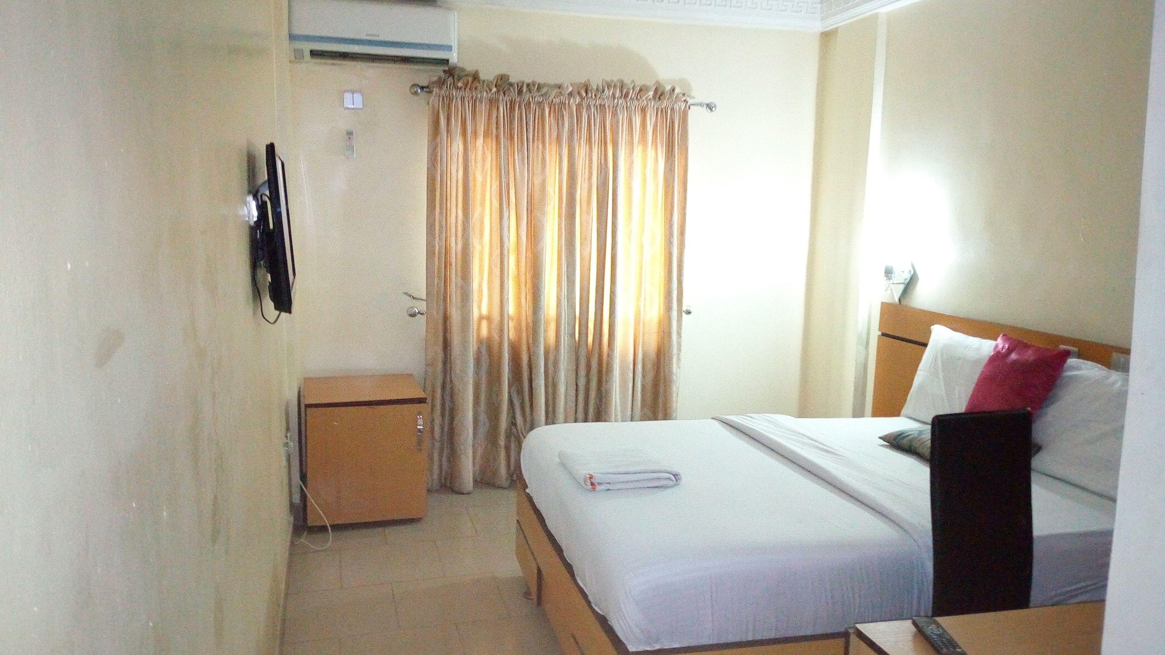 Quarto de hotel com cama, mesa de cabeceira, guarda-roupa, cortina e ar condicionado.