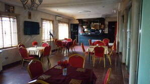 A dining area with tables and chairs, a kitchen in the background, and a television on the wall. - D'Czars Hotel & Suites (Lagos)