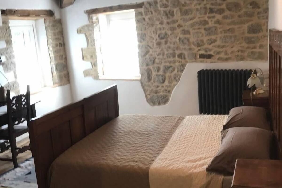 A bedroom with a stone wall, a wooden bed, and a radiator.