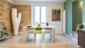 Un espace repas avec une table et des chaises blanches, un mur en pierre et une grande sculpture abstraite.
