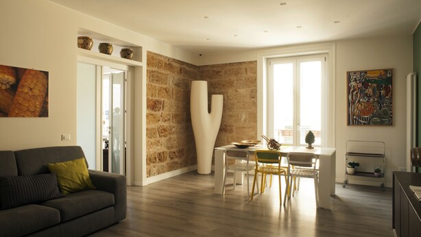 Un salon moderne avec un canapé gris, une table à manger avec des chaises, un vase blanc et un mur en pierre.