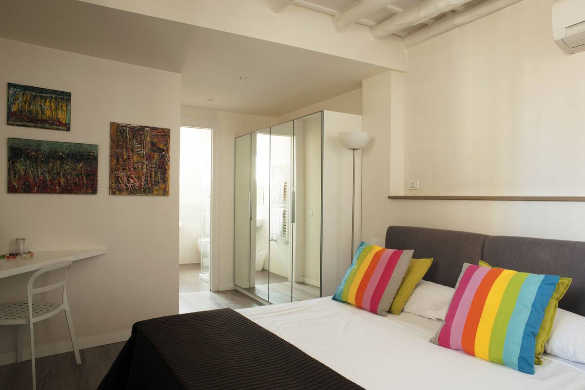 A modern hotel room with a bed, a desk, and a glass partition.