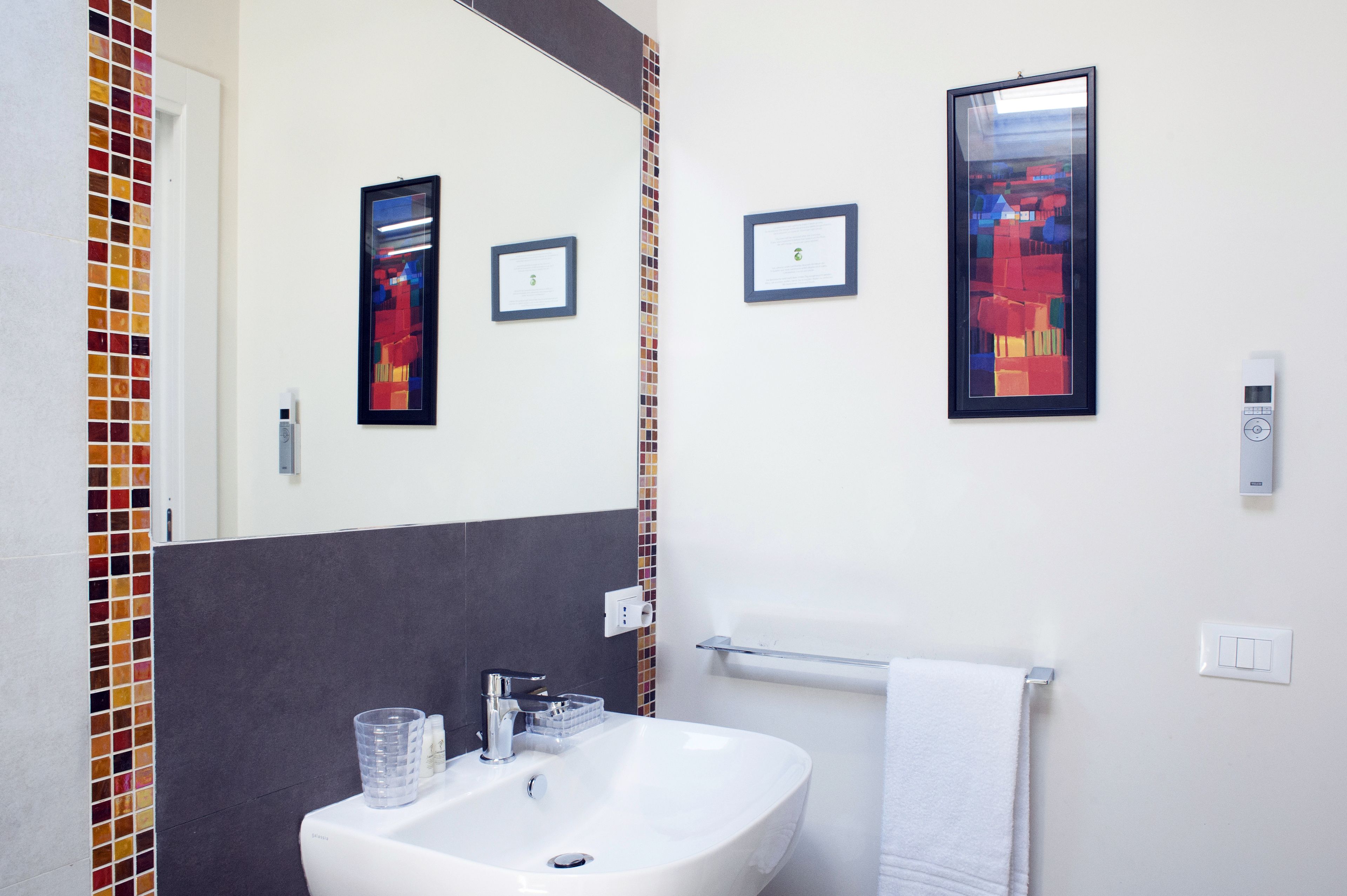 A bathroom with a white sink, a mirror, and two framed artworks on the wall.