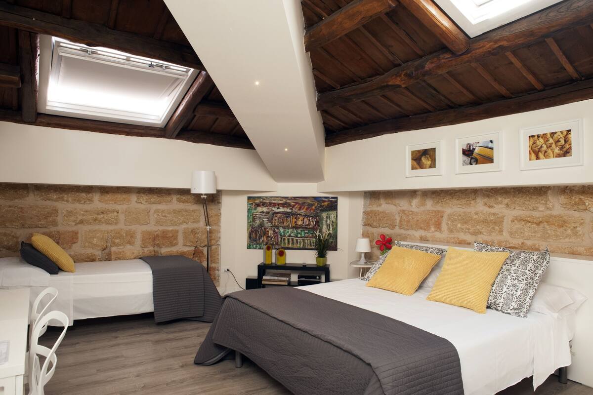 A bedroom with two beds, a stone wall, a skylight, and a painting.