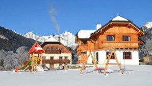 Un chalet de madera con balcón, una zona de juegos con tobogán y un telesilla al fondo.