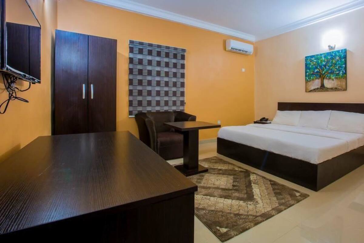 A hotel room with a bed, a desk, a chair, a wardrobe, and a painting on the wall.