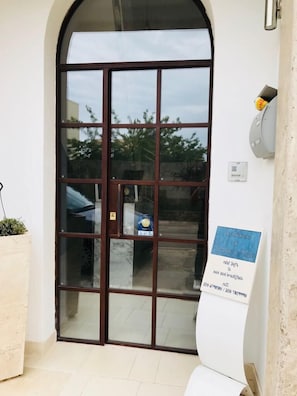 Una puerta de cristal con marco marrón, una planta pequeña en maceta a la izquierda y un letrero a la derecha.