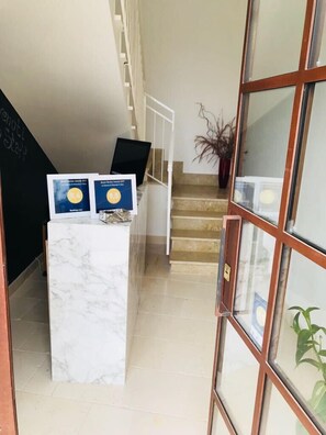 Un área de recepción con mostrador de mármol, una escalera y un amplio ventanal con una planta.
