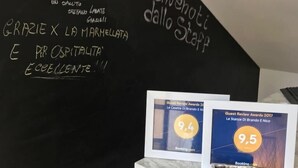 A hotel reception desk with a blackboard displaying a welcome message and guest review awards. - Le Stanze Di Brando E Nico (Tricase)