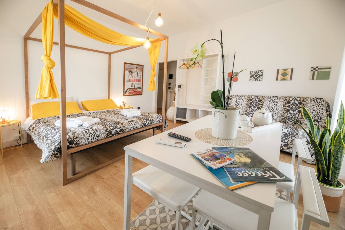 Une chambre à coucher moderne avec un lit à baldaquin, un canapé, une table à manger et une plante en pot.