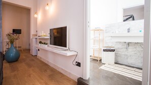 A modern living room with a flat-screen TV, white shelves, a blue vase, and a wooden floor. - Le Stanze Di Brando E Nico (Tricase)