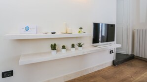 A modern living room with a flat-screen TV on a white shelf, a small table with candles, and several potted plants. - Le Stanze Di Brando E Nico (Tricase)