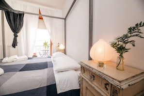 Habitación de hotel con cama, mesita de noche con lámpara, un jarrón con flores y vistas al balcón exterior.