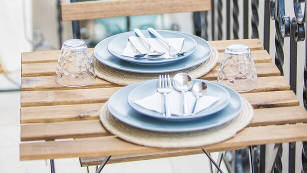 A wooden table set with plates, cutlery, and glasses on a balcony with a metal railing. - Le Stanze Di Brando E Nico (Tricase)