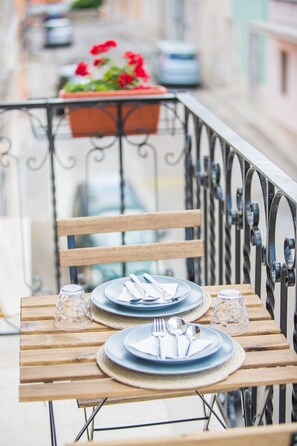Une table en bois, dressée avec des assiettes, des couverts et des verres, sur un balcon doté d’une rambarde en métal.