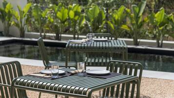 An outdoor dining area with metal chairs and a table set for two, near a swimming pool.