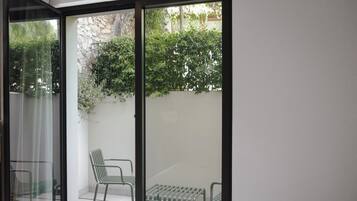 Una stanza con un letto e una porta scorrevole in vetro che dà su un patio esterno con due sedie verdi e una panca.