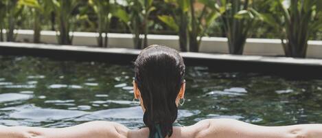 Una persona descansando junto a una piscina, con agua y vegetación al fondo.