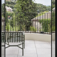 A balcony with a metal bench, a view of a green landscape, and a stone wall.