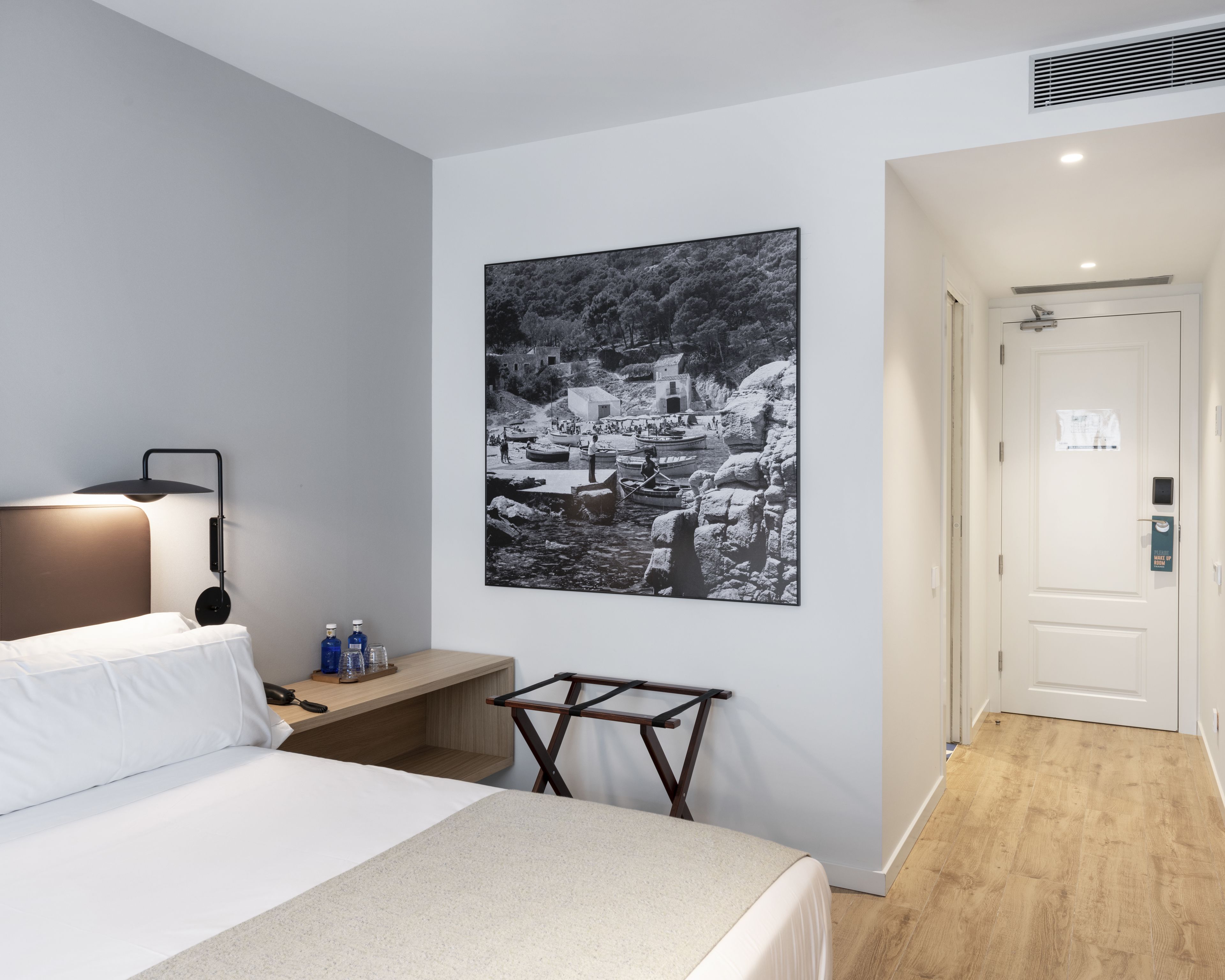 Habitación de hotel con cama, mesita de noche, lámpara y una fotografía grande en blanco y negro en la pared.