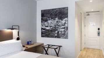 Habitación de hotel con cama, mesita de noche, lámpara y una fotografía grande en blanco y negro en la pared.