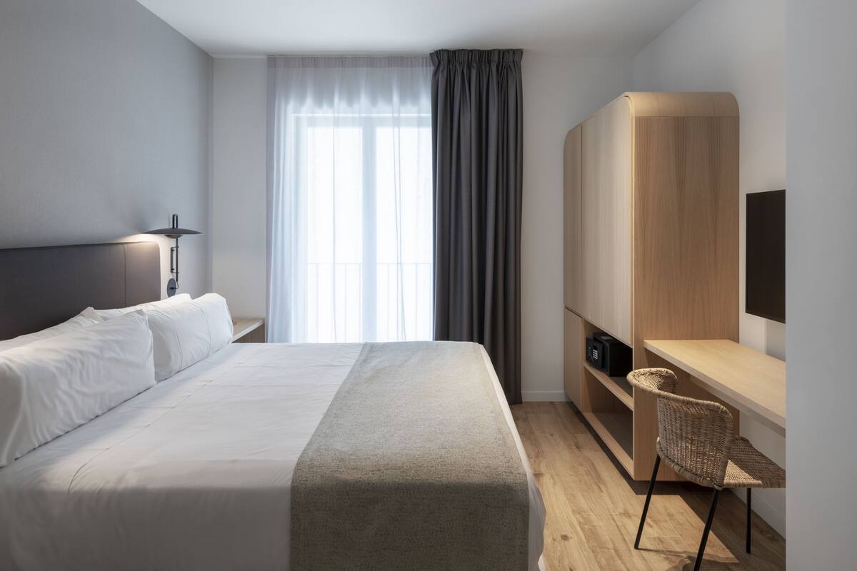 Una habitación de hotel moderna con cama, escritorio, silla y televisor.