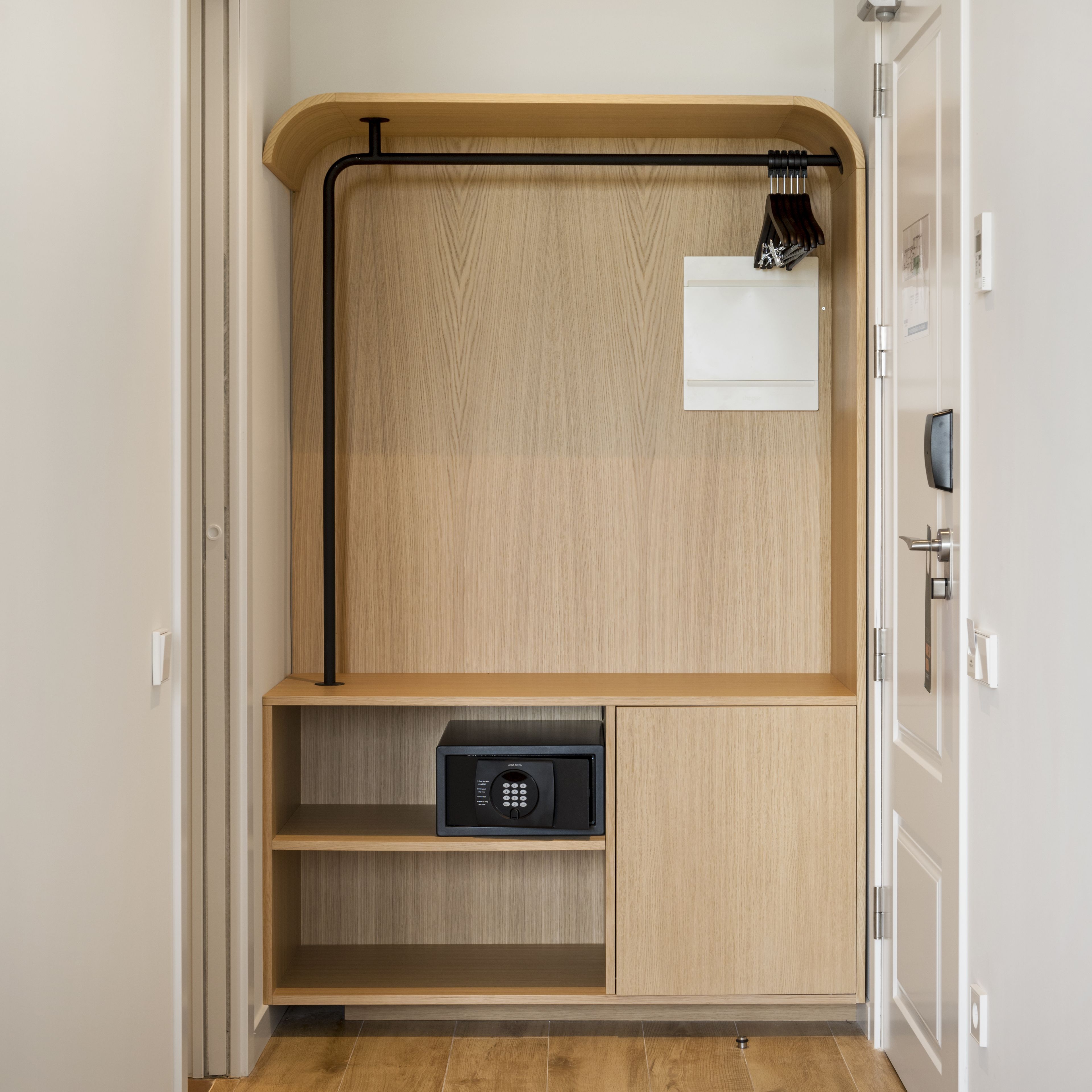 Een moderne, minimalistische kamer met een houten garderobe, een klein plankje en een geïntegreerde kluis.